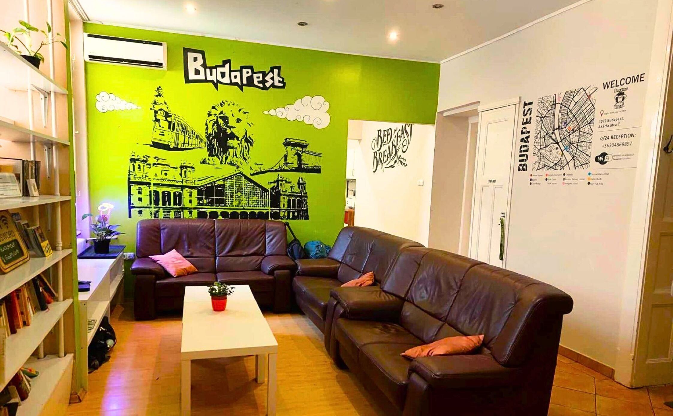 Una habitación con una pared verde, un sofá de cuero negro, una mesa blanca y una estantería.