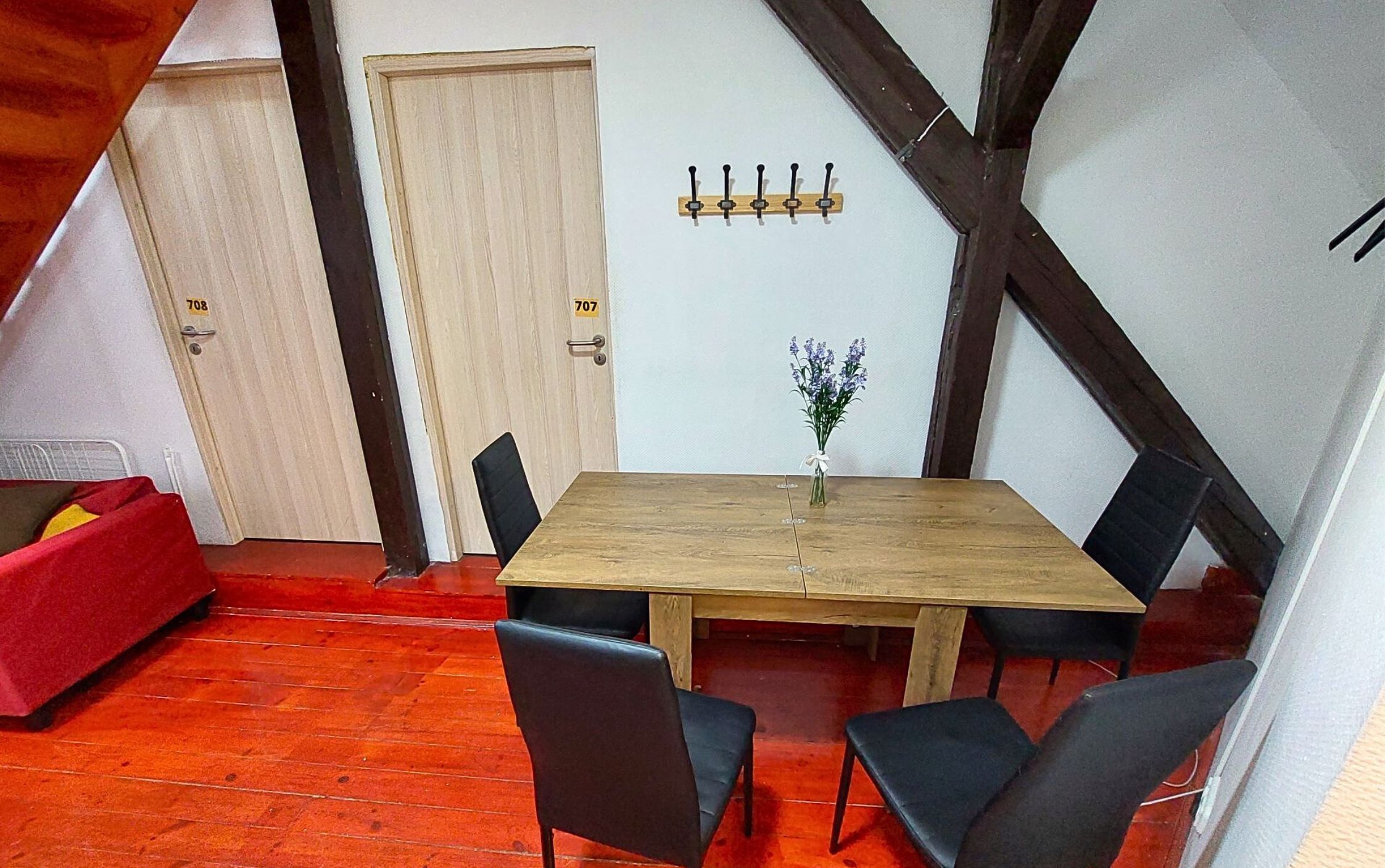 Un comedor con una mesa de madera y sillas negras, un sofá rojo y un perchero de pared.