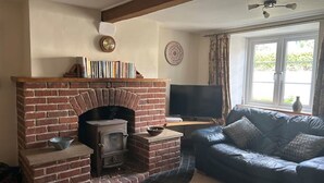 Ein Wohnzimmer mit Kamin aus Ziegelsteinen, einer Ledersofa, einem Flachbildfernseher und einem großen Fenster mit Vorhängen.