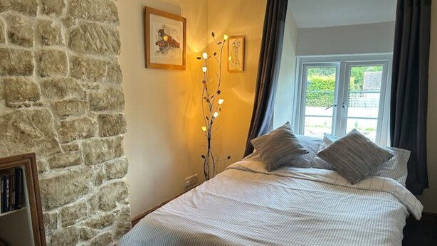 Ein Schlafzimmer mit Steinwand, einem Bett mit gestreifter Bettwäsche, einem Nachttisch mit Lampe und einem Fenster mit Vorhängen.