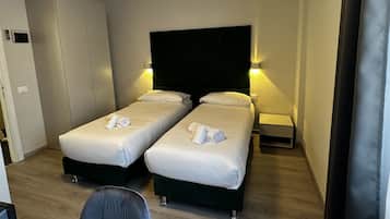A hotel room with two single beds, a desk with a chair, a flat-screen TV, and a ceiling light.