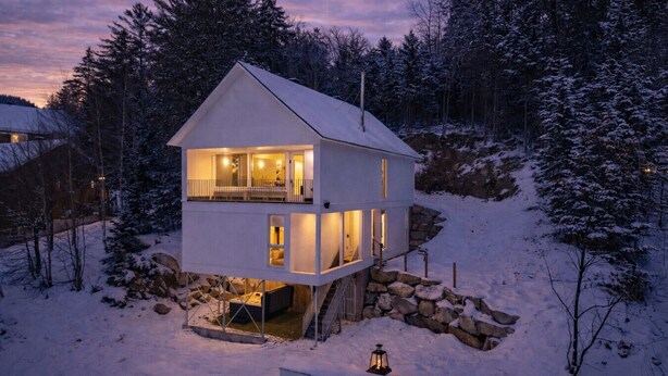 En toetages hytte med balkon, omgivet af sneklædte træer.