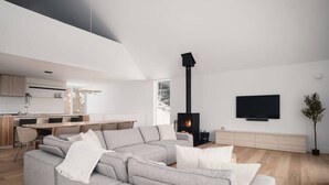 En moderne stue med en modulsofa, en pejs, et spiseområde og et fjernsyn monteret på væggen.