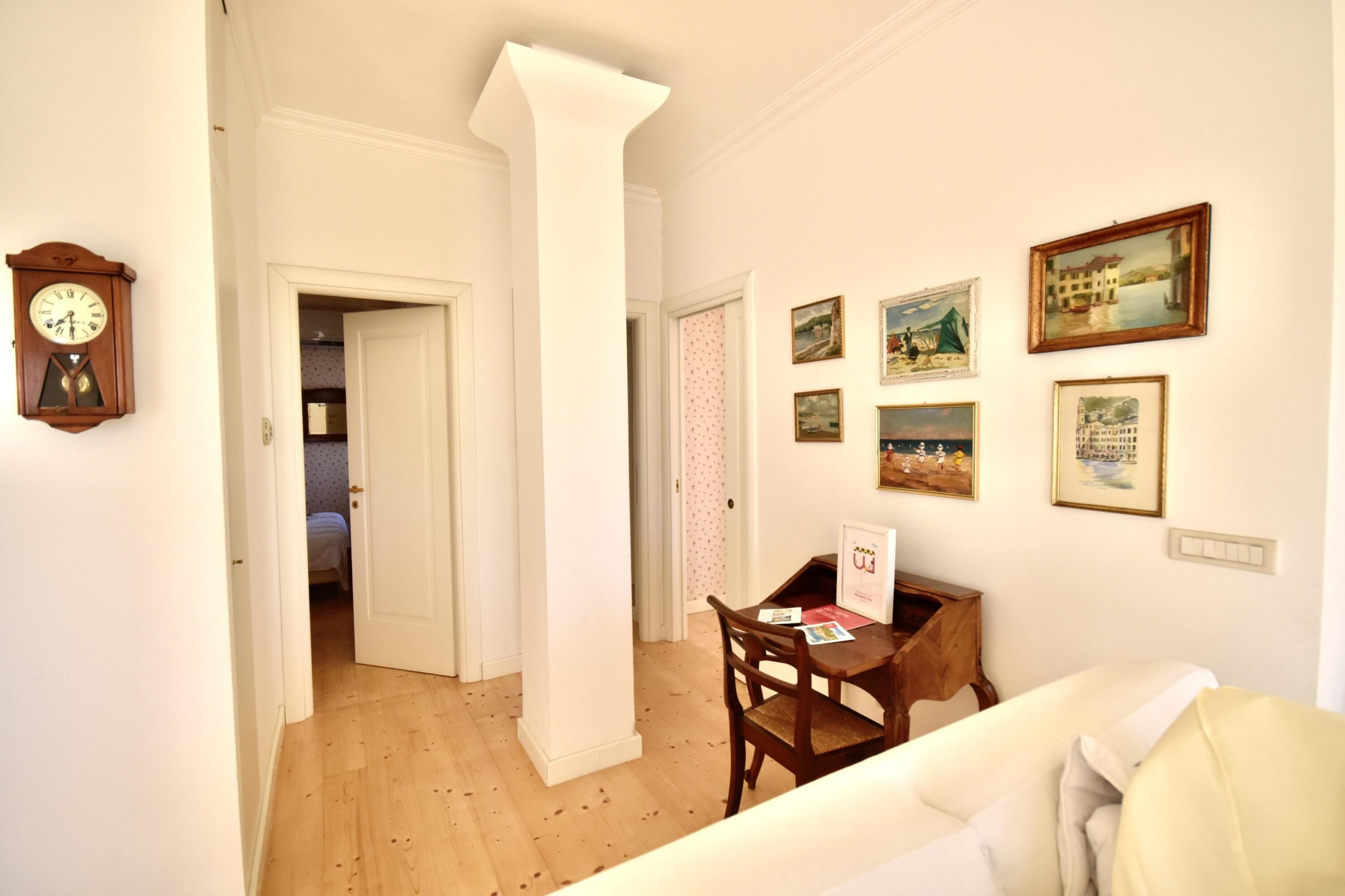 Una habitación con piso de madera, paredes blancas, una silla de madera, una mesita con un letrero y un reloj en la pared.
