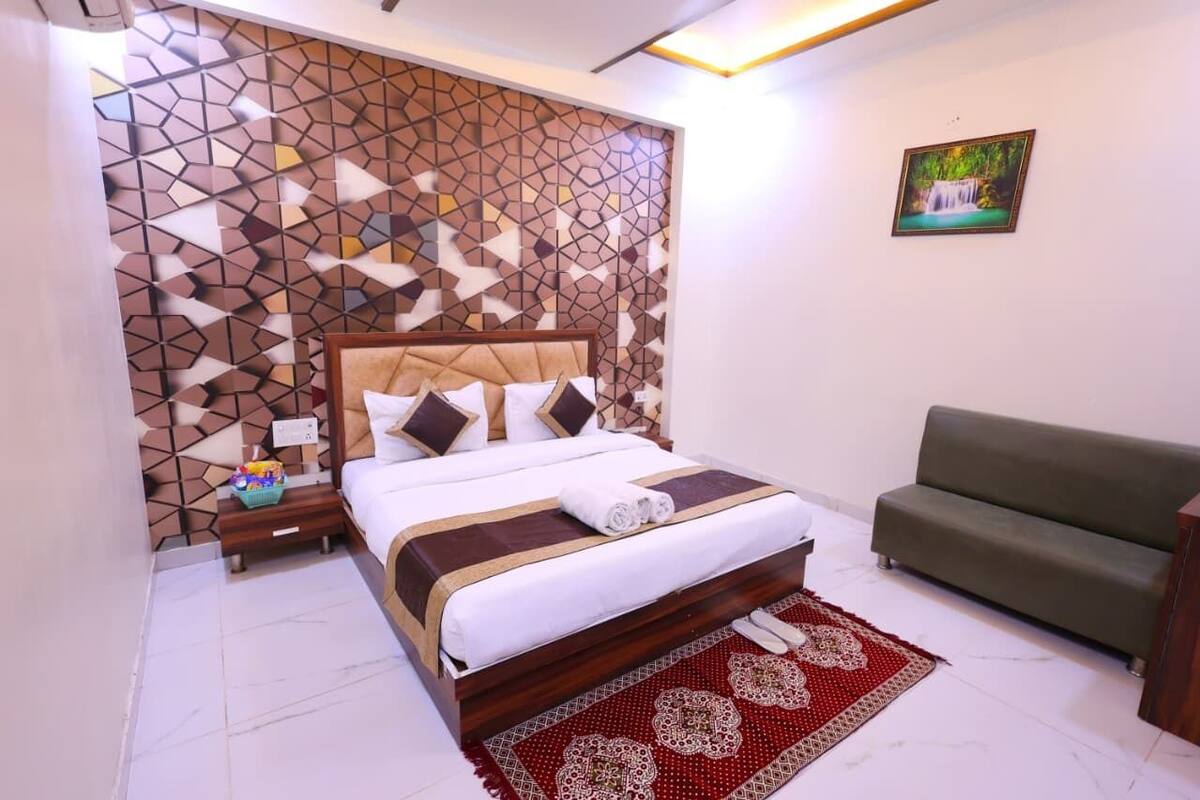 A neatly arranged bedroom with a bed, a green sofa, a patterned wall, and a framed picture on the wall.