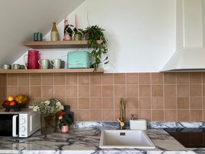 A kitchen with a microwave, toaster, sink, and a shelf with various kitchen items and plants. - Plantation´s Villa - Funchal Seaside Villas (Funchal)
