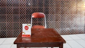 A wooden table with a red chair in front of a patterned tile wall. A sign with text is placed on the table.