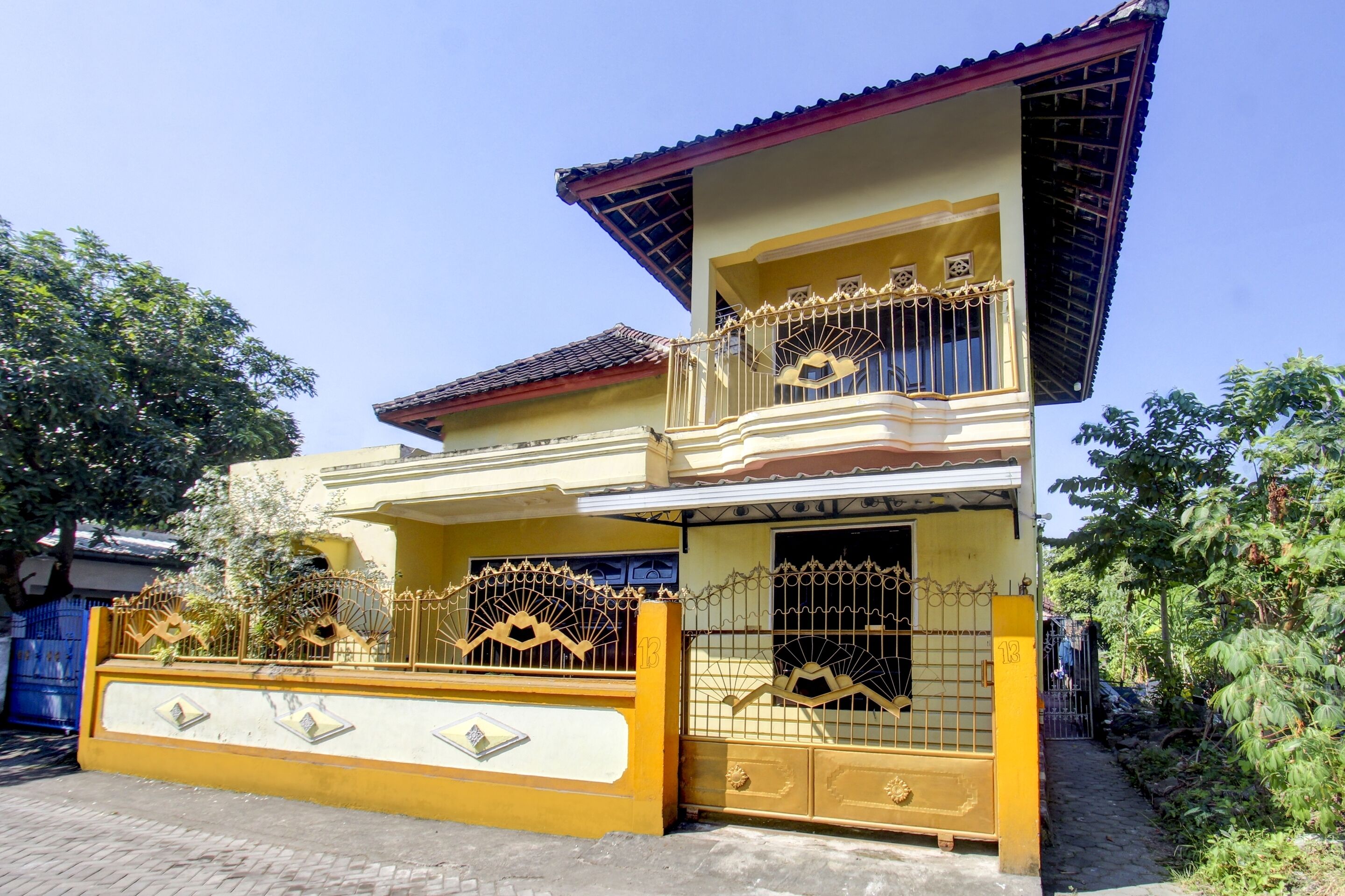 A two-story house with a yellow facade, a balcony with ornate metal railings, and a gated entrance.