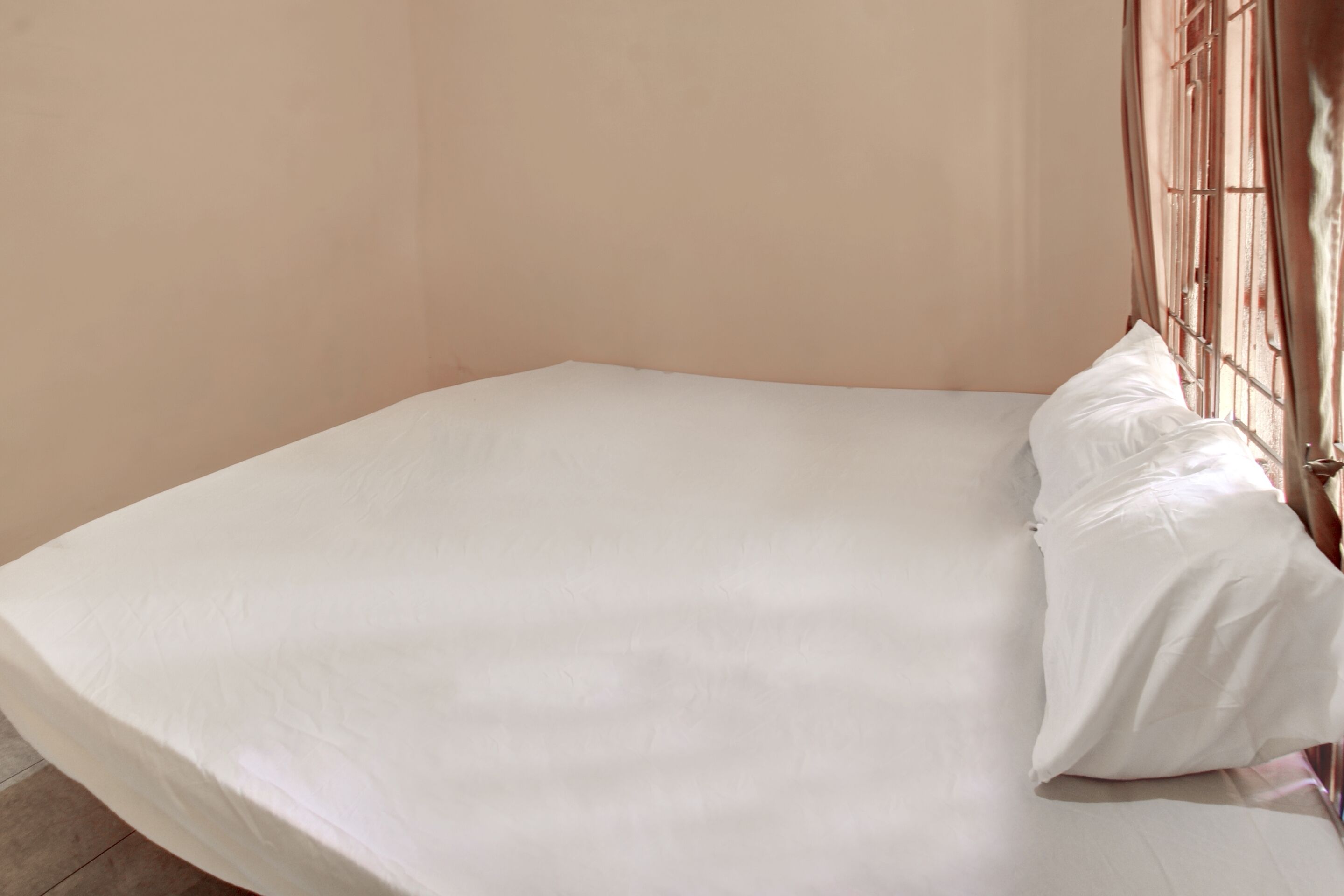 A single bed with a white mattress and pillows, a metal headboard, and a plain wall.