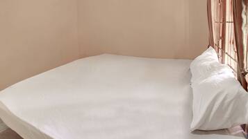 A single bed with a white mattress and pillows, a metal headboard, and a plain wall.