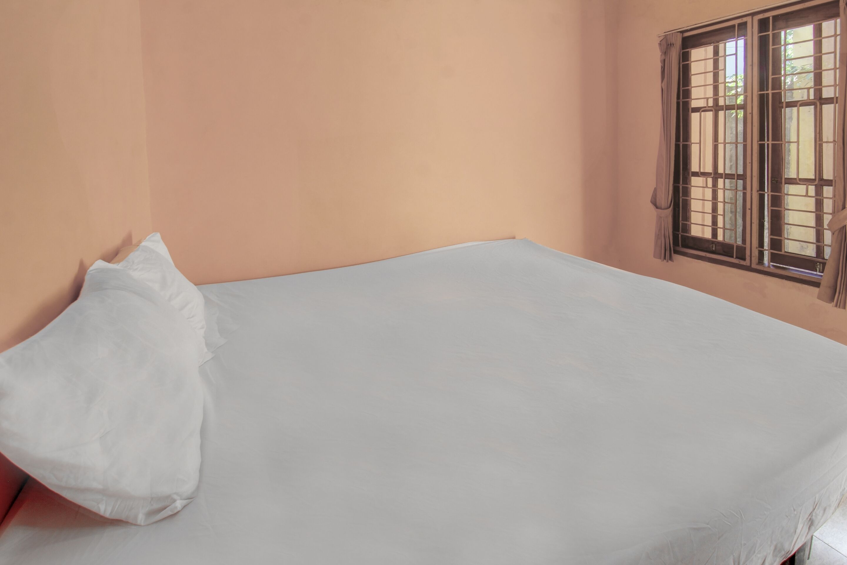 A room with a single bed, a window with bars, and a plain wall.