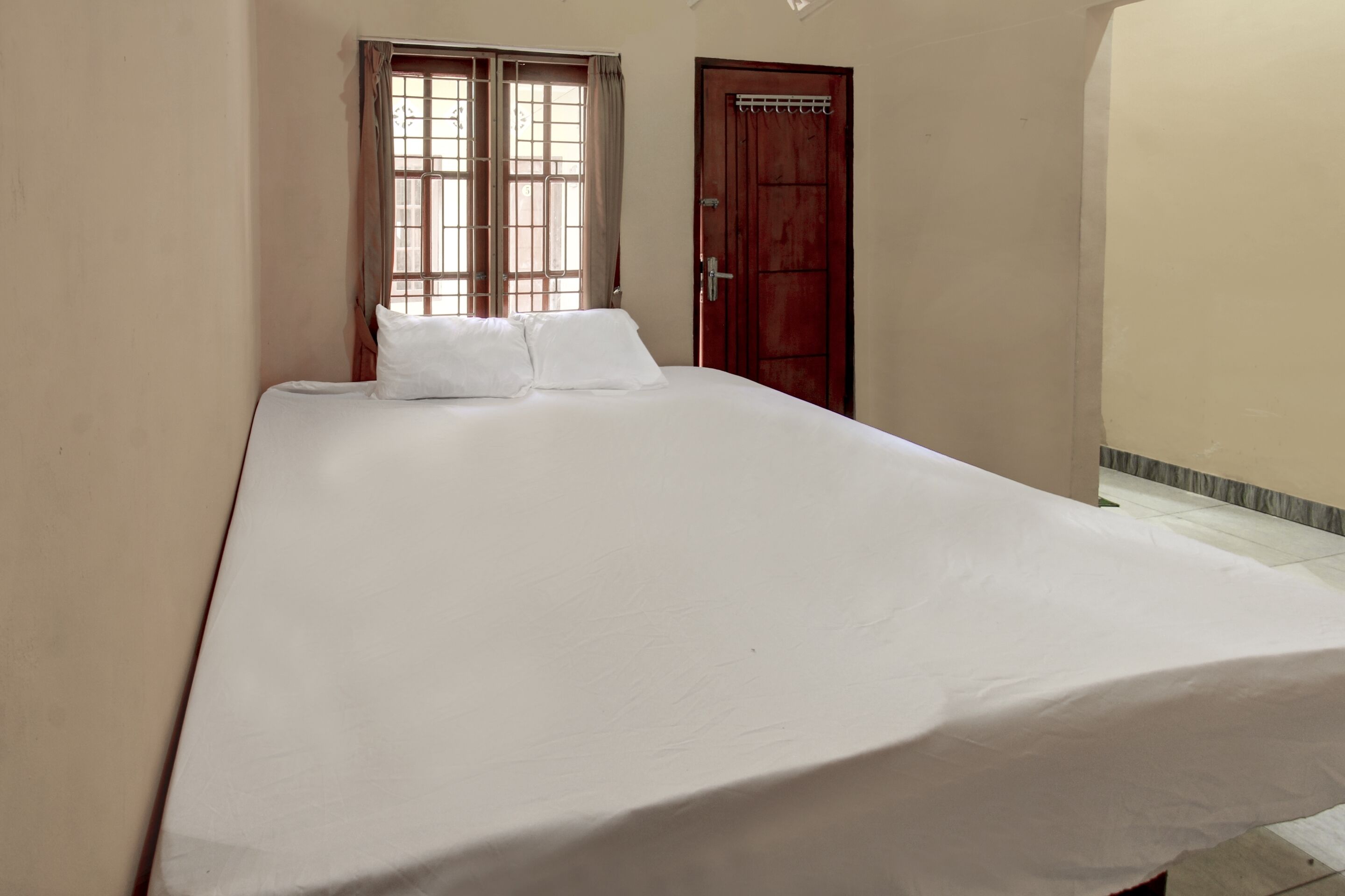 A bedroom with a large bed, a window with curtains, and a wooden door.