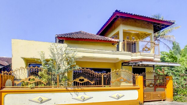 A two-story house with a balcony, a gated entrance, and a yellow exterior.