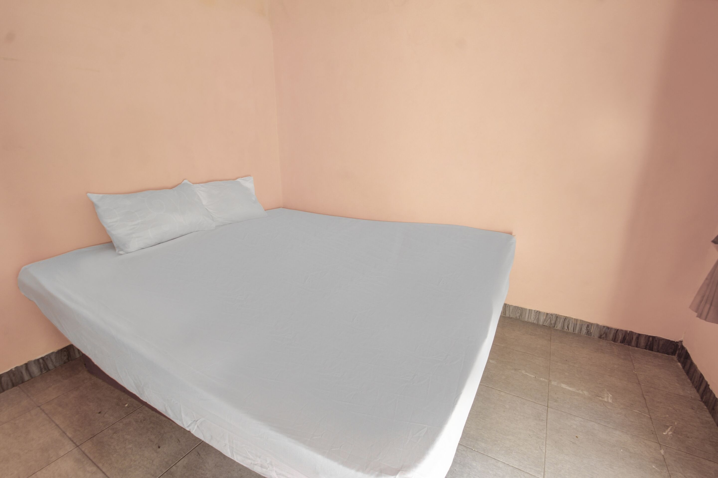 Un lit simple dans une chambre aux murs de couleur pêche et au sol carrelé.