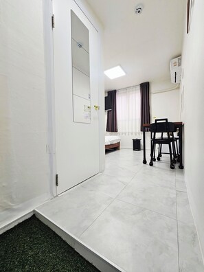 A hotel room with a bed, a desk, and a chair. There is a window with curtains and an air conditioning unit on the wall. - Anjin's Guest House (Mokpo)