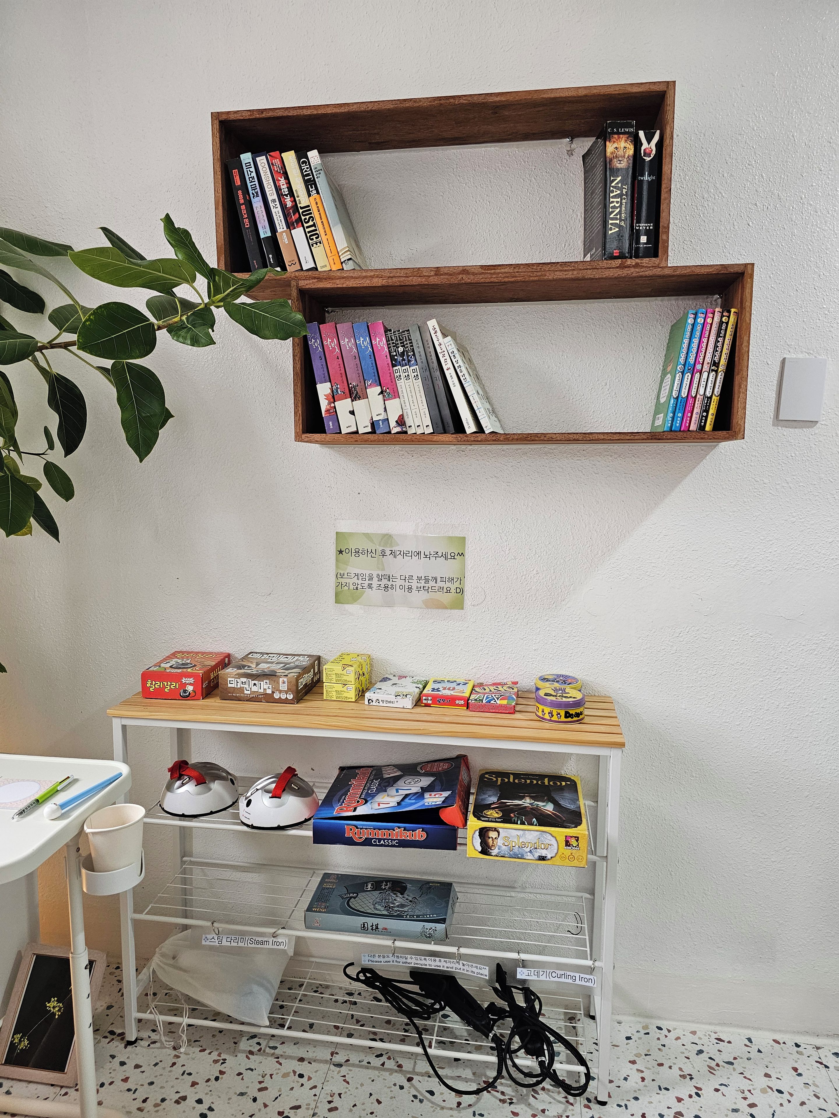 A room with two wooden bookshelves, a table with various items, and a plant.