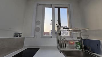 A compact kitchen with a window, a built-in stove, a sink, and a drying rack.