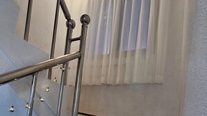 A staircase with wooden steps and metal railings, leading to a room with a window and a light fixture. - Anjin's Guest House (Mokpo)