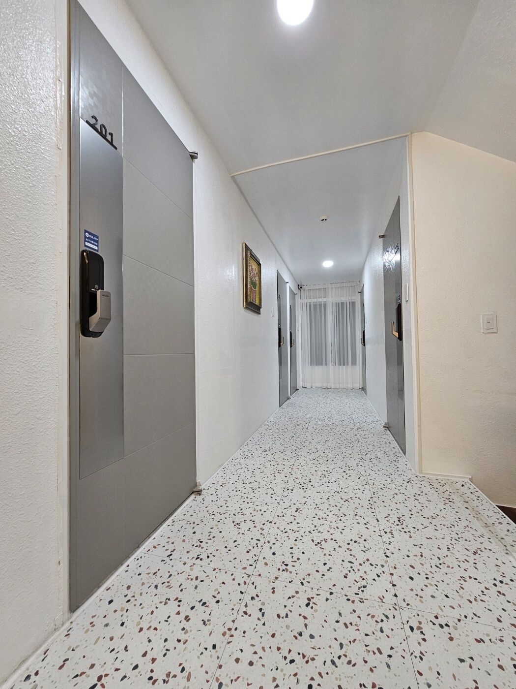 Un pasillo con piso moteado, una puerta con el símbolo de número y un lector de tarjeta de seguridad.