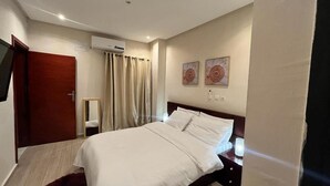 A hotel room with a bed, a nightstand, a mirror, a door, and an air conditioning unit. - We Offer you a Lovely 1-bed Apartment in Abidjan (Abidjan)