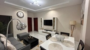 A modern living room with a sofa, coffee table, TV, and dining area. - We Offer you a Lovely 1-bed Apartment in Abidjan (Abidjan)