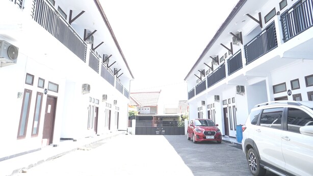 Una calle estrecha bordeada por edificios blancos con balcones y un coche rojo estacionado a la derecha.