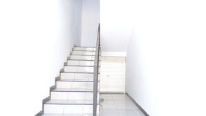 Una escalera con baldosas blancas y barandilla de metal que lleva a una puerta cerrada.
