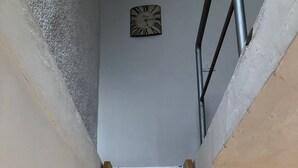 Une échelle en bois mène à un escalier étroit, et une horloge est accrochée au mur.