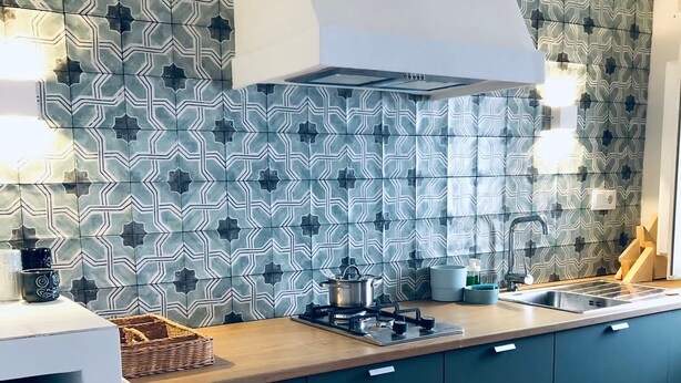 Une cuisine moderne avec des carreaux décoratifs sur le mur derrière l’évier, une cuisinière à gaz et des armoires de couleur turquoise.