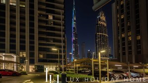 A nighttime view of a modern building complex with illuminated windows and a prominent tower in the background. - LUX The Downtown Zabeel View Suite 2 (Dubai)