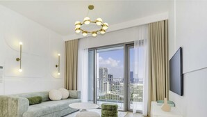 A modern living room with a sofa, a round coffee table, a TV mounted on the wall, and a balcony with a city view. - LUX The Downtown Zabeel View Suite 2 (Dubai)