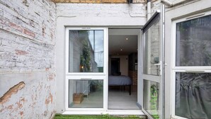 A small, enclosed outdoor space with a white brick wall, a grassy area, and a bed visible through a glass door leading into a room. - 1-bed Flat in West London, Sleeps 2 (London)