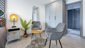 A modern living room with a grey armchair, a small round table, a floor lamp, a mirror, and a wardrobe. - 1-bed Flat in West London, Sleeps 2 (London)