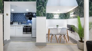 A modern kitchen with white cabinets and a blue patterned backsplash, a dining area with a white table and chairs, and a potted plant. - 1-bed Flat in West London, Sleeps 2 (London)