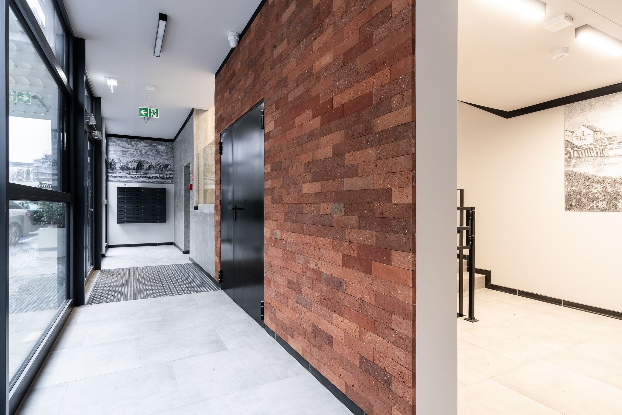Un pasillo moderno con pared de ladrillo, puerta de vidrio y un mural.