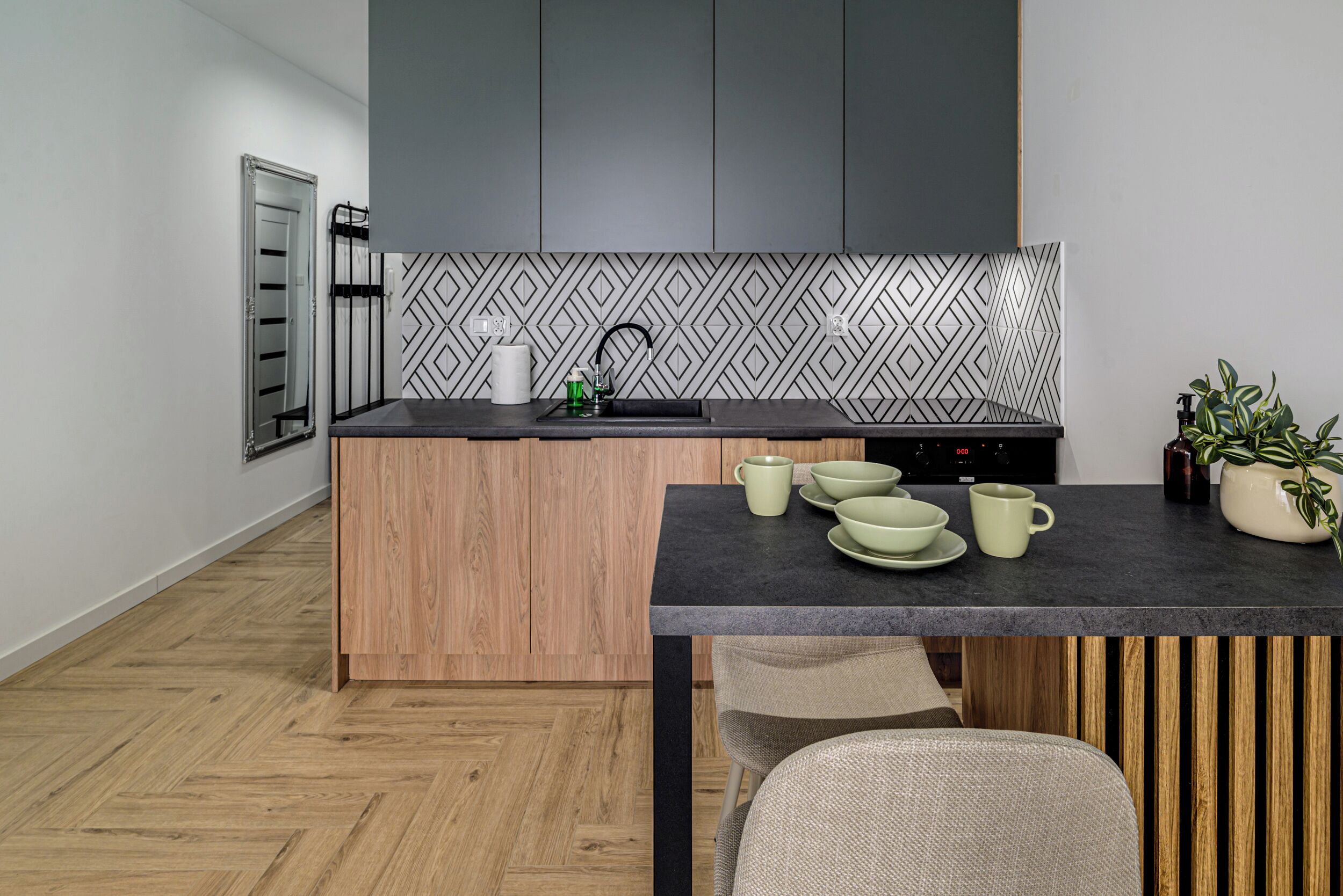 A modern kitchen with a herringbone-patterned backsplash, a wooden island, and a black countertop.