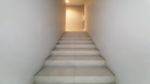 A narrow, well-lit staircase with a plain wall on either side, leading to a door at the top. - OYO Life 92770 Cozy Puri 22 (Jakarta)