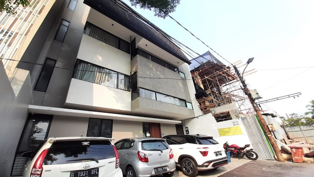 A multi-story building with a modern architectural design, featuring a parking area with several cars and a motorcycle. - OYO Life 92770 Cozy Puri 22 (Jakarta)