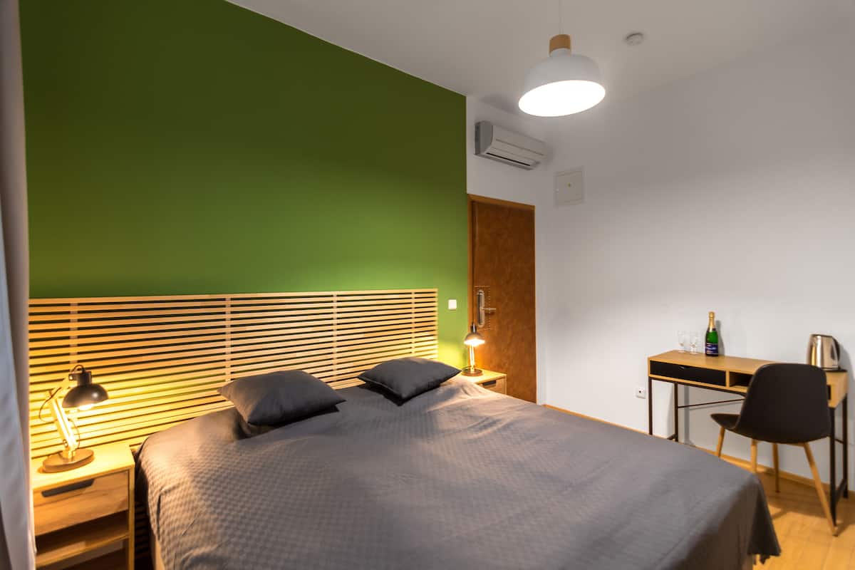 A bedroom with a bed, bedside table, lamp, and a desk with a chair.