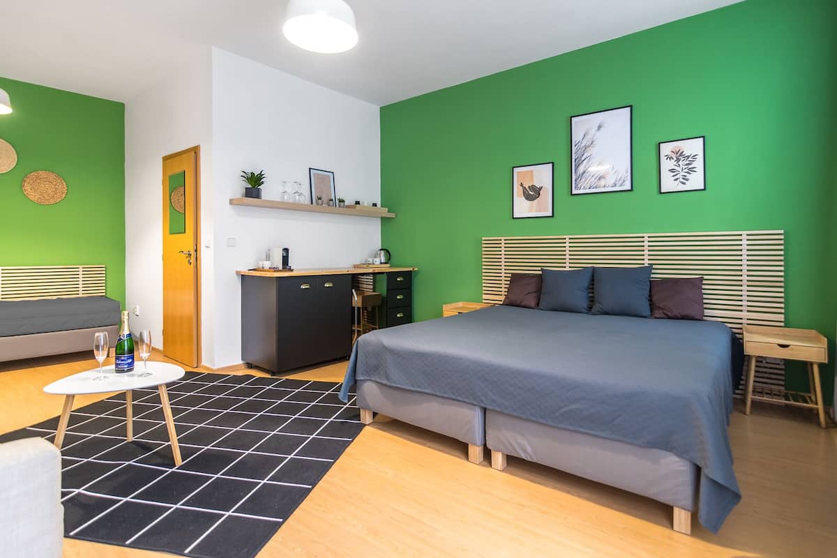 A modern bedroom with a bed, a small kitchenette, and a green accent wall.