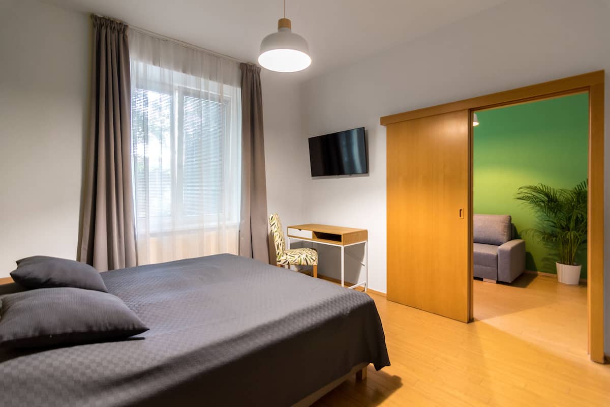 A bedroom with a bed, a desk, a chair, a TV, and a green wall.