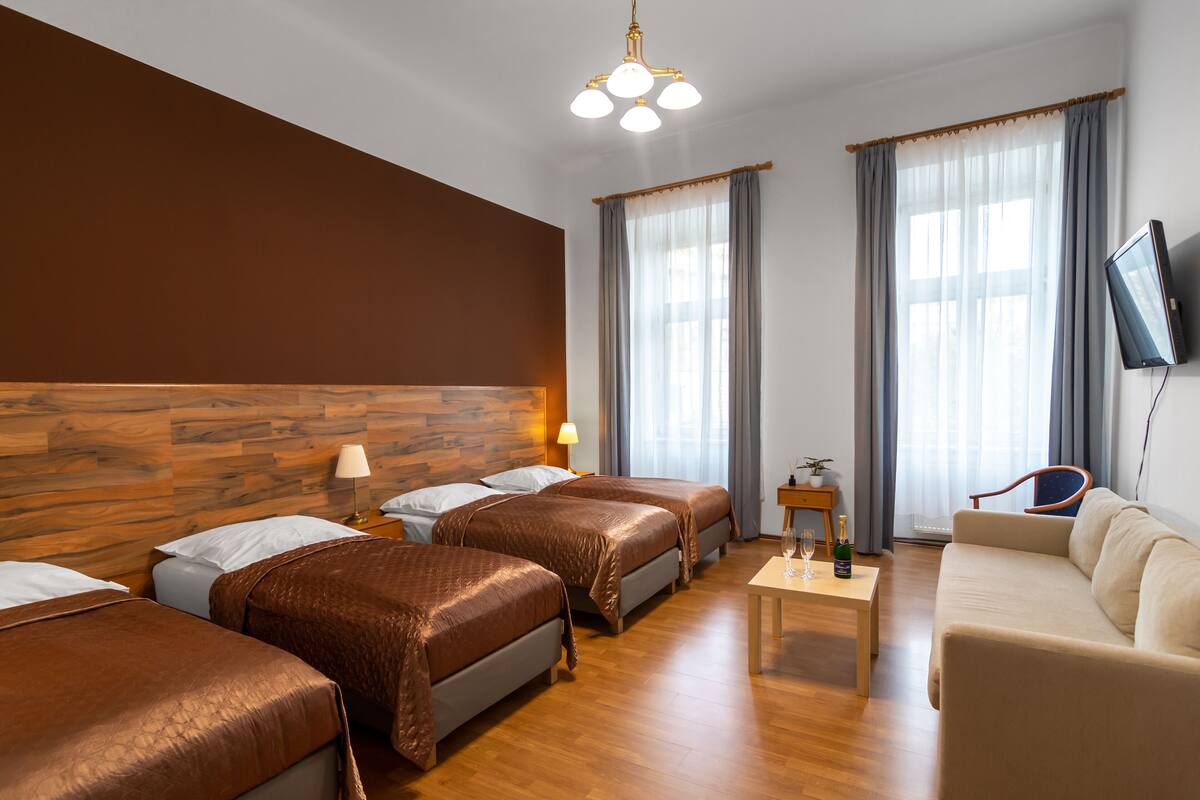 A hotel room with three beds, a sofa, a television, and a small table with a bottle and glasses.