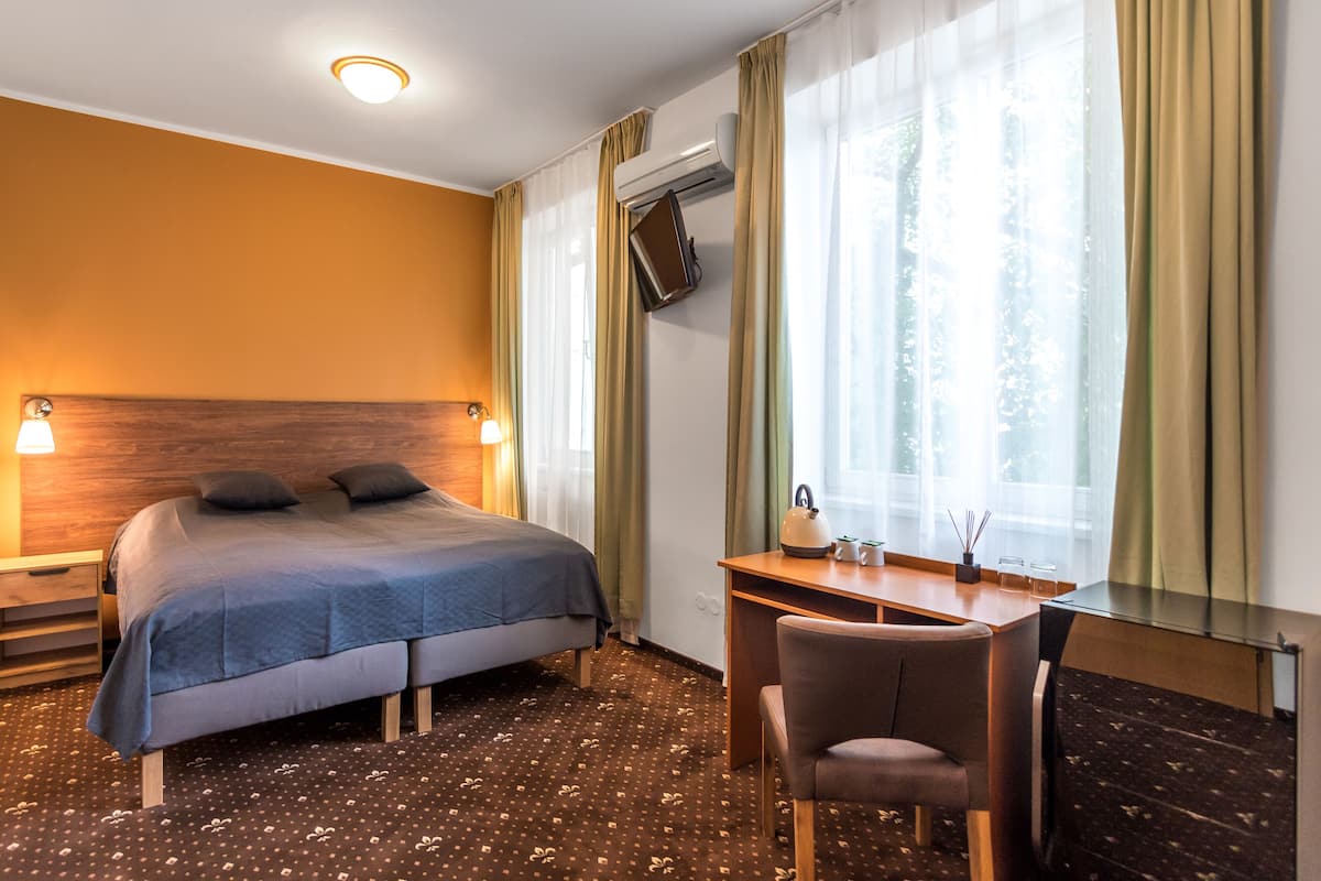 A hotel room with a bed, desk, chair, and a TV mounted on the wall.