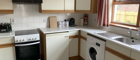 A compact kitchen with a stove, oven, washing machine, and sink.