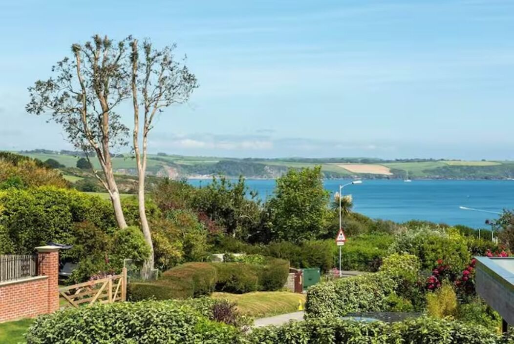 A coastal landscape with a view of the sea, a tree, and a brick wall.