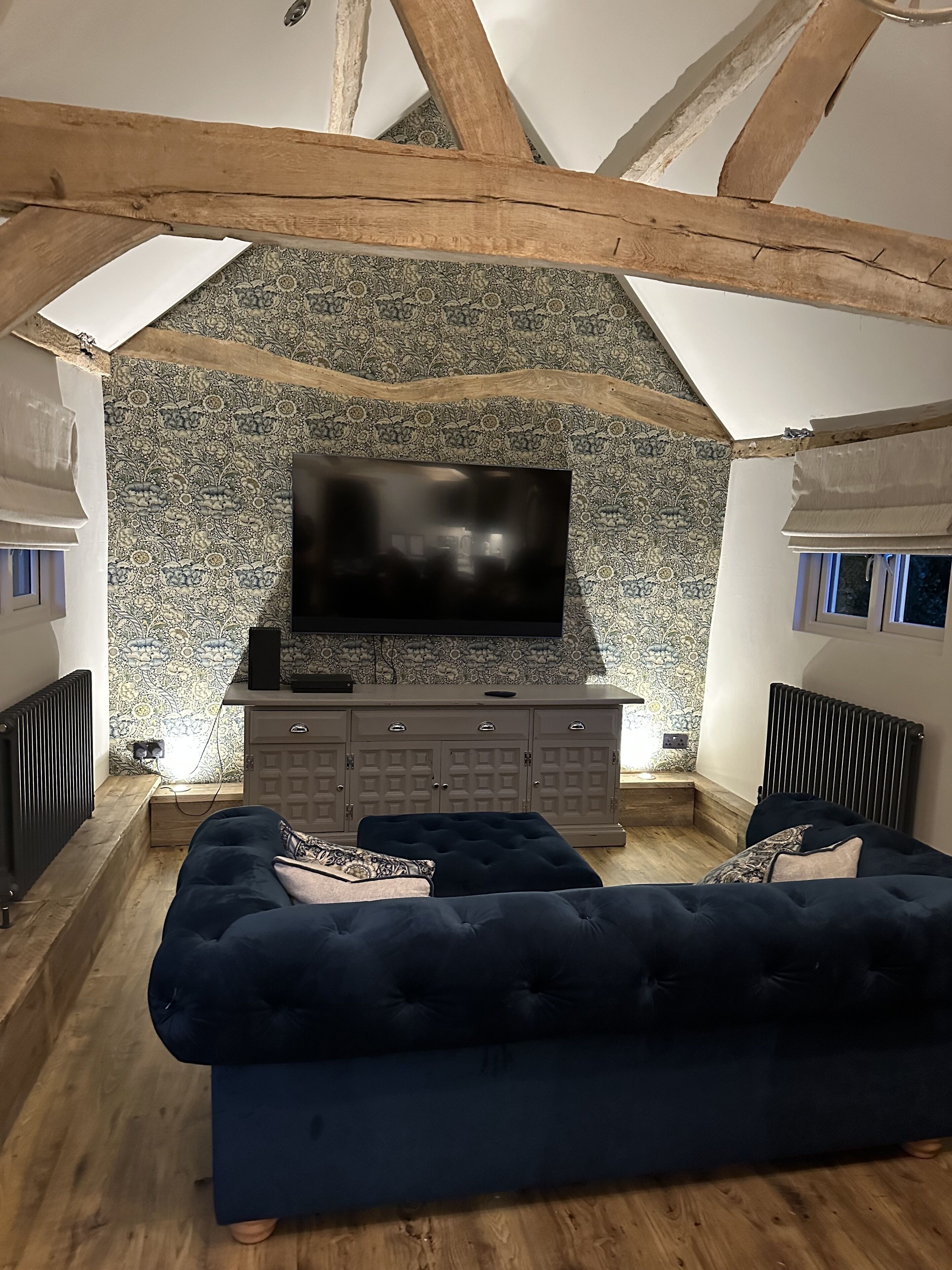 Una sala de estar acogedora con un sofá azul oscuro, un televisor de pantalla plana sobre un muro estampado y un mueble de madera debajo.