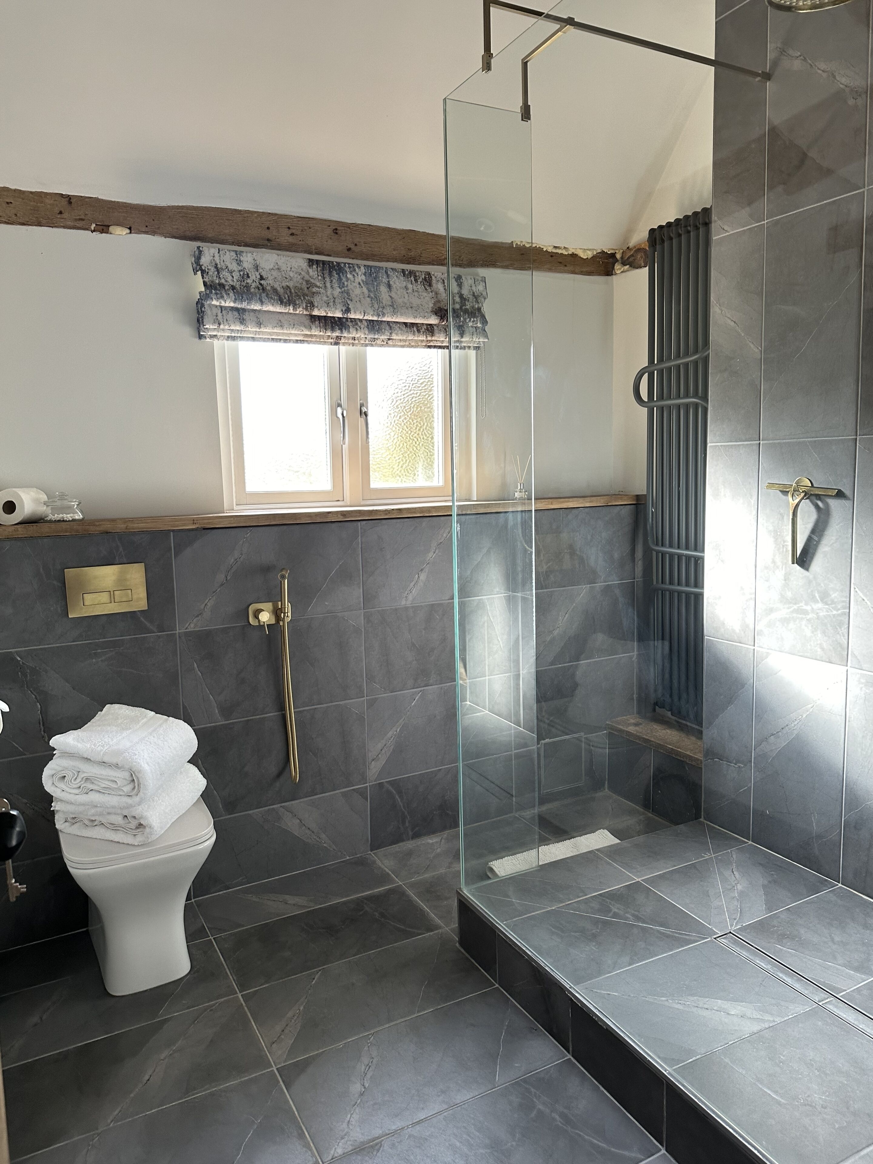 A modern bathroom with a glass-enclosed shower, a toilet, and a window with a frosted glass panel.