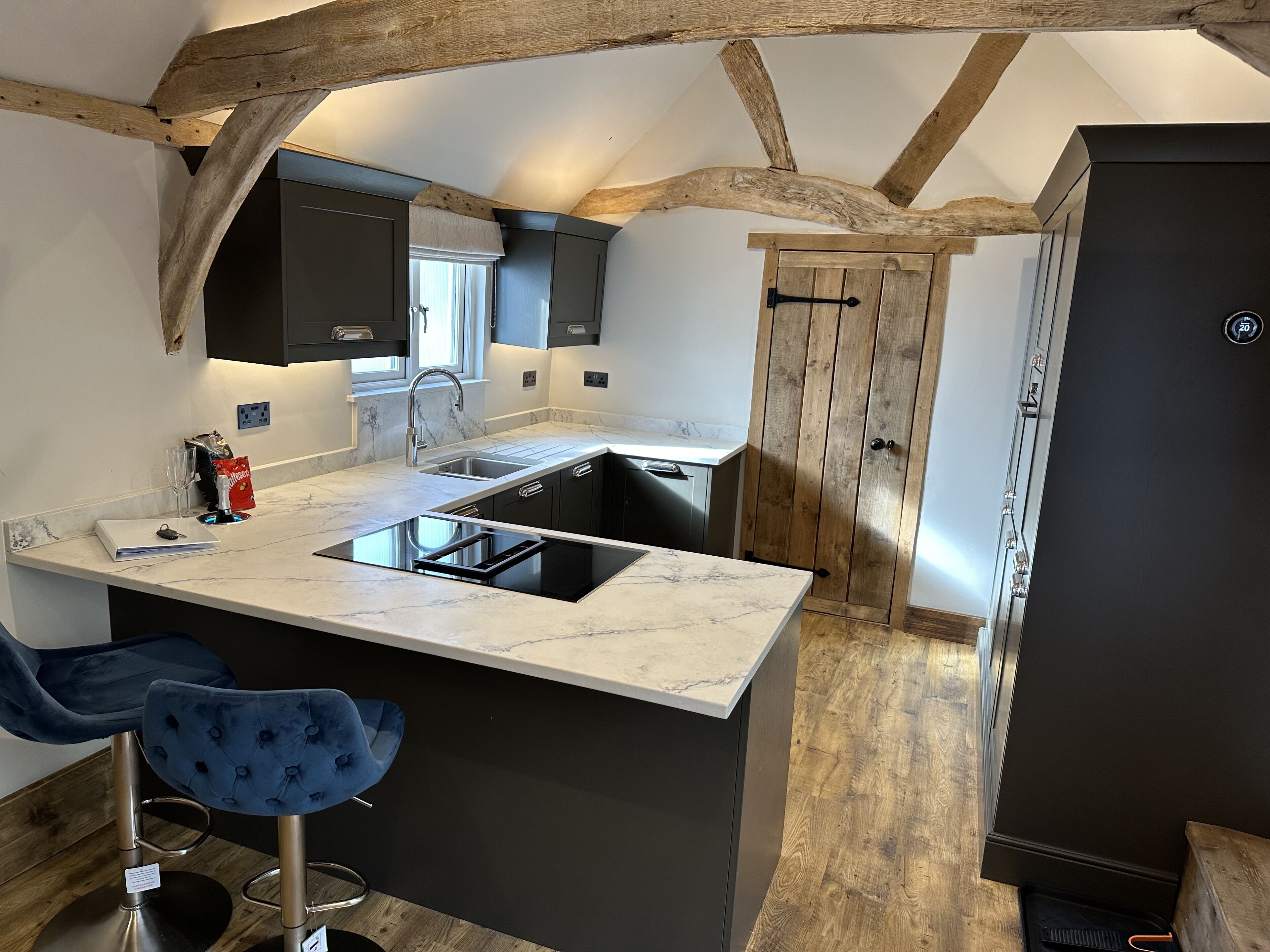 Une cuisine moderne avec un plan de travail en marbre, des meubles noirs et un plafond en bois.