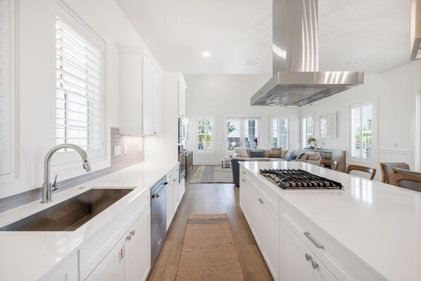 Una cocina moderna con armarios blancos, una campana extractora de acero inoxidable y una isla grande con estufa integrada.