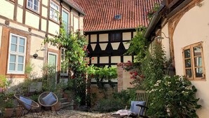 A courtyard with cobblestone flooring, two wicker chairs, a wooden rocking chair, and a small table with a newspaper. - Erholung mit Hof-idylle & Kamin im Einmaligen Denkmal von 1477, 120qm, Parkpl (Quedlinburg)